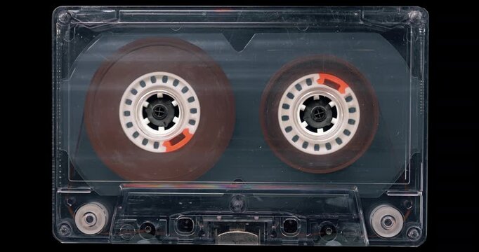 Old Transparent Audio Cassette with Reels Turning.
Exposed magnetic tape reels rotate smoothly inside a clear unlabeled cassette.