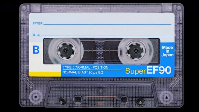 Audio Cassette Rewinding on Black.
Two reels spin as magnetic tape winds inside a vintage cassette.