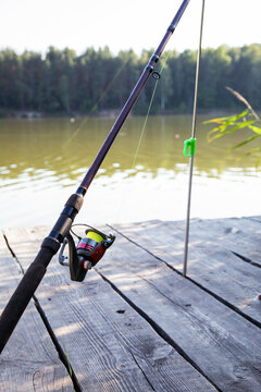 Fishing rod with spinning reel on a wooden pier near the river at sunny summer day