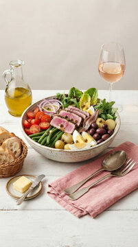 Classic Ni&ccedil;oise salad with seared tuna, eggs, tomatoes, and potatoes, and a glass of ros&eacute; wine on a rustic wooden table