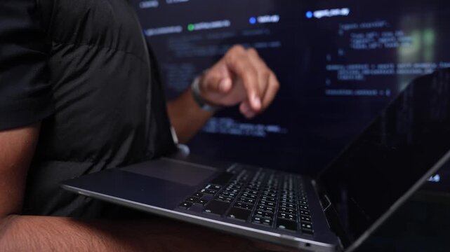 Detailed view of hands working on a laptop keyboard with a programming interface displayed in the background