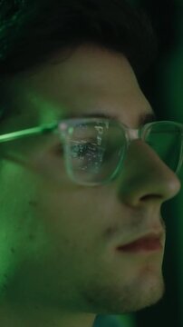 Close-up profile of a young male editor working at night, with code reflecting in his glasses