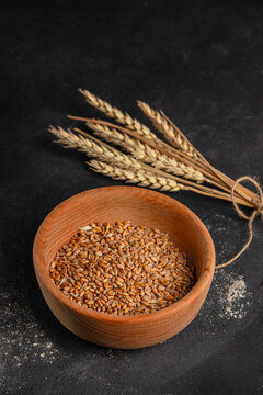 Bowl of whole wheat grains placed on a dark surface with a bundle of dried wheat stalks arranged beside it, showcasing natural food elements and textures. copy space