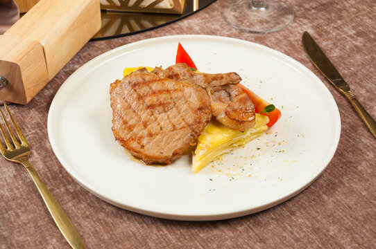 Grilled pork steak served over layered potato gratin with red pepper garnish on white plate