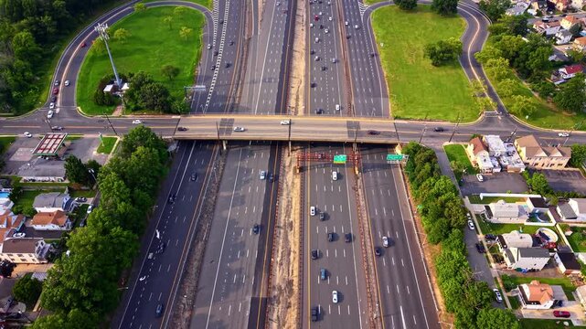 Direct overhead view of straight highway lanes and green fields, United States. Drone perspective of parallel roadways running through suburban neighborhood and parkland. Garden State Parkway