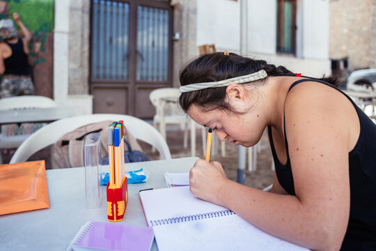 Young Woman Drawing in Sketchbook Outdoors Beside Senior Artist Painting Street Mural