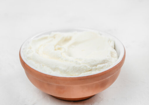 Creamy white yogurt in a round copper bowl placed on a light textured surface, showcasing its smooth and thick consistency for culinary use
