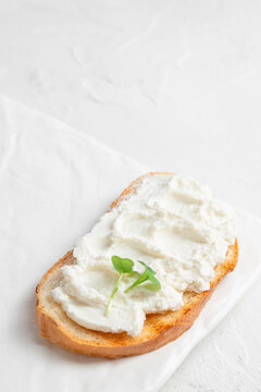 Toasted bread slice topped with creamy ricotta cheese and fresh microgreens on a white plate, showcasing a simple yet elegant food presentation. copy space.