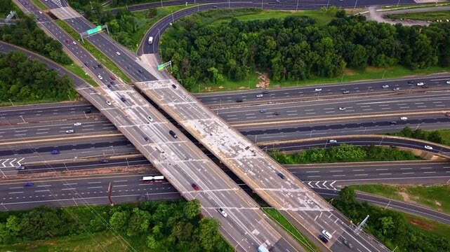 Aerial view of highway interchange overpass. Overhead drone shot of concrete bridge crossing multilane freeway with cars, trucks and green forest border. Garden State Parkway