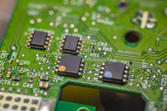 Close-up view of a green printed circuit board featuring multiple integrated circuits, resistors, and soldered connections, showcasing intricate electronic components and pathways