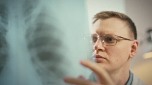 Doctor carefully examines patient's lung x-ray on bright clinic screen, scanning shadows for disease. This focused examination supports diagnosis, underscoring imaging's vital role respiratory care