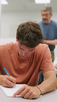 Young male student writing an exam in classroom