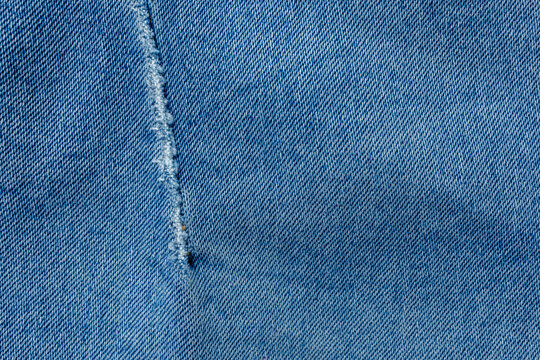 Worn blue denim fabric with distressed seam texture