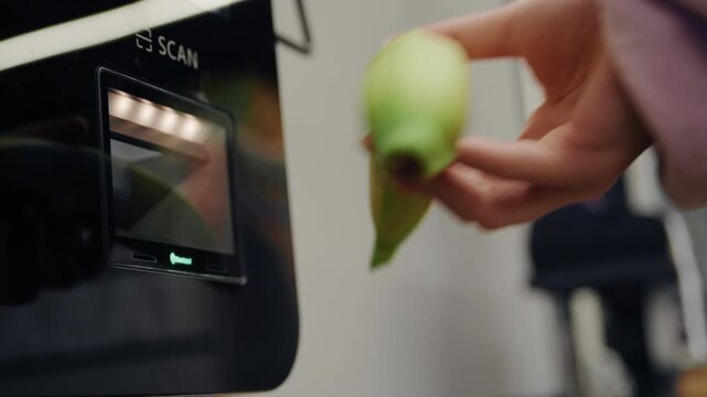 Person's hand scanning an apple and a banana at a self-service checkout machine in a grocery store