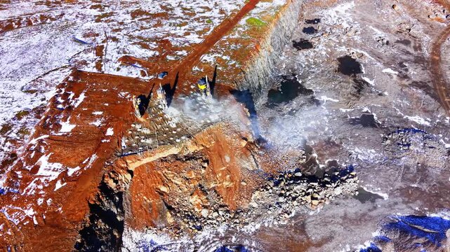 Overhead view of quarry drilling machinery. Directly above shot captures yellow drill rigs, dust clouds and rust colored terraced rock.