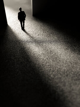 Silhouette of a man in a suit walking into a bright light from darkness