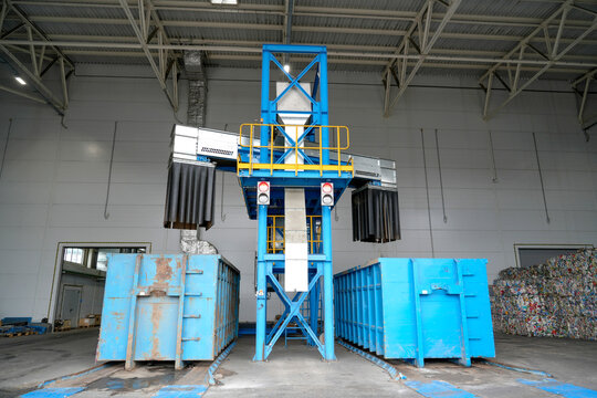 Blue industrial equipment handles materials, with collection bins and recycled bales awaiting further processing