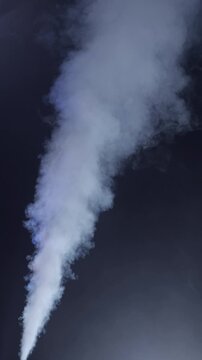 White Smoke Jet Rising on Dark Background. Dense plume shoots upward, expands and disperses into swirling smoke against a dark blue background.