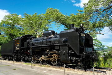 Vintage black steam locomotive parked outdoors under blue sky © Takuya Sato