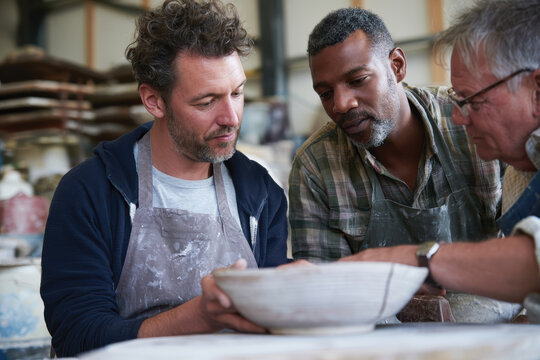 Three men engaged in pottery collaboration, working hands-on to shape clay, which highlights the importance of teamwork and shared creativity in artistic processes.