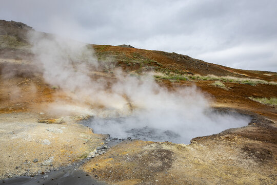View of Seltun Geothermal Area with steaming mud pots and vibrant mineral-rich volcanic soil under a cloudy sky in Grindavik, Hafnarfjardarkaupstad, Iceland.