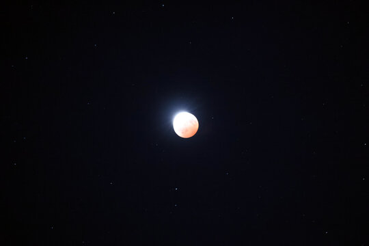 Sturgeon Full Moon with partial eclipse glows with a distinctive red orange hue against a deep black night sky with visible stars, captured on August 28, 2026.