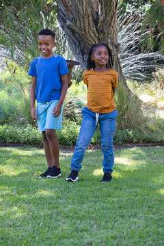 Two African youth males standing and smiling in bright T-shirts and shorts near large tree planter