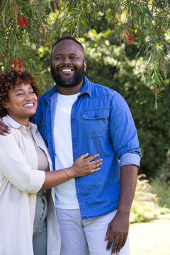 African American couple standing under tree in park with red blooms, wearing denim and beige