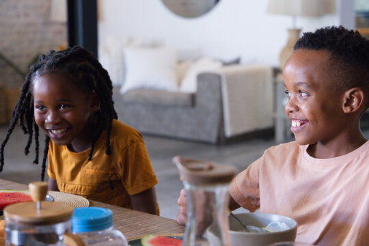 African American children smiling and sharing breakfast at home dining table with bowls and pitcher