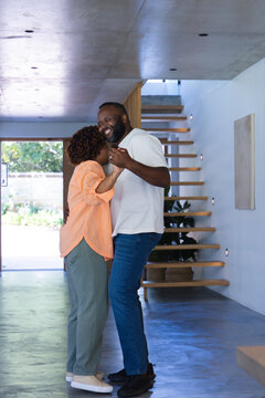 African American couple dancing, laughing in modern hallway by floating staircase, potted plant