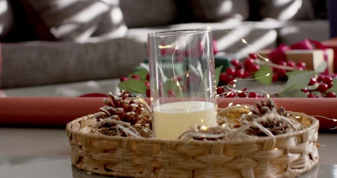 Camera is pulling back showing wicker tray with candle on table, arm reaching arranging gifts