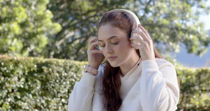 Woman in twenties picking up headphones on bench, inspecting, placing over ears