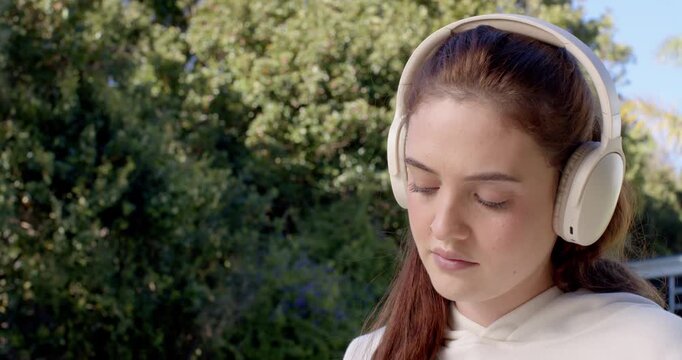 Female wearing light hoodie and white over-ear headphones keeping downward gaze on porch