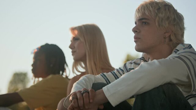Multiethnic teenagers sitting outdoors together and looking into distance. Ideal for youth lifestyle advertisements, mental health awareness campaigns, and social diversity promotions