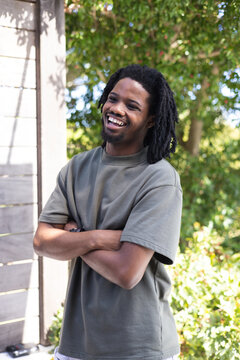 African American man standing in backyard by wooden wall wearing green shirt smiling, showing watch