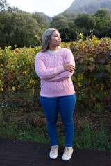 Naklejka premium African American woman standing on wooden boardwalk in vineyard, wearing pink sweater and jeans
