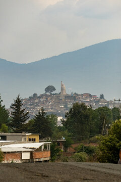 View of the Monumento a Jose Maria Morelos y Pavon atop the island of Janitzio, with hillside houses, lush trees, and mountains in the background in Janitzio, Michoacan, Mexico.