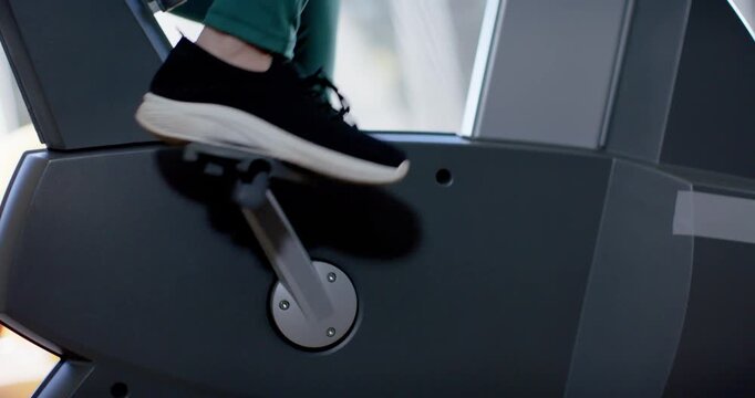 Right foot pressing down and pedaling for exercise, legs in sneakers cycling on machine near window
