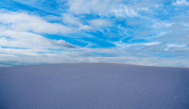 View of a vast sand dune under a bright blue sky with scattered clouds in Barcelona, Catalonia, Spain.
