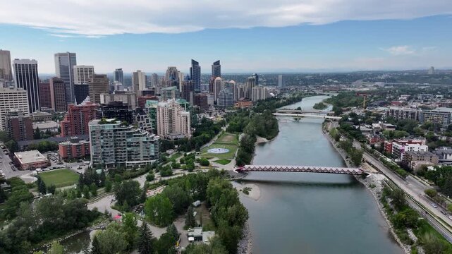 panning 180&deg; left from Peace Bridge along Skyline of Downtown Calgary ( Alberta, Canada)  to Centre St Bridge, with Prince&rsquo;s Island Park and Bow River below and skyscrapers in front - 4k aerial video