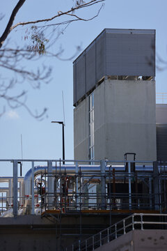View of a modern data center facility featuring industrial metal pipes and scaffolding against a clear blue sky in Sydney, New South Wales, Australia.