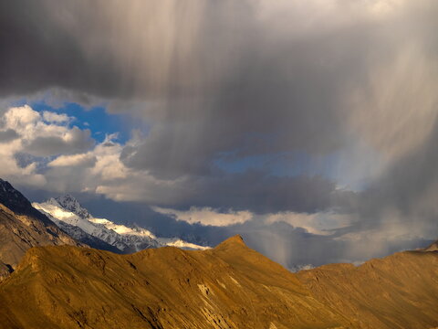 View of the dramatic landscape at Hopper Glacier View point with snow-capped peaks illuminated by sunlight under a stormy sky in Hunza Nagar, Gilgit Baltistan, Pakistan.
