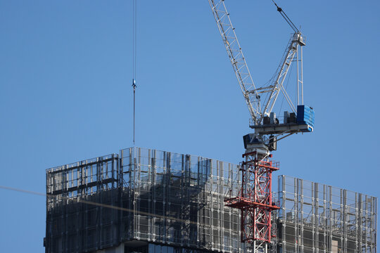 View of a tall construction crane towering over a modern building under construction with scaffolding and protective mesh in Parramatta, New South Wales, Australia.