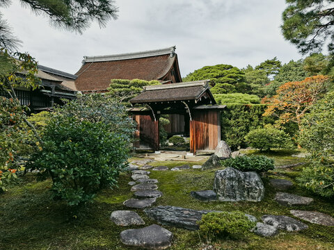 View of a traditional wooden temple gate and stone path surrounded by manicured trees and mossy garden in Kyoto, Kyoto, Japan.