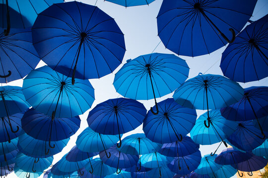 Blue umbrellas create a layered canopy with patches of sky between them, colorful outdoor decoration, creative festival background.