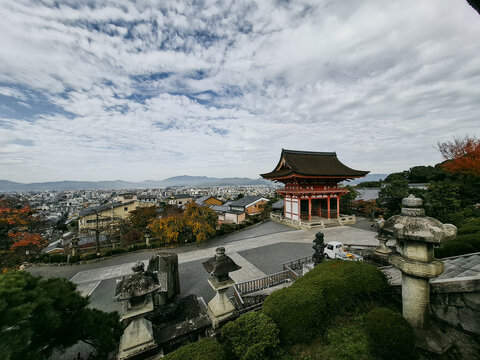 View of the historic Kiyomizu-dera temple with traditional wooden architecture, stone lanterns, and lush trees overlooking the city skyline under a cloudy sky in Kyoto, Kyoto, Japan.