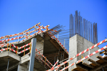 Fototapeta premium Unfinished concrete building structure with exposed rebar columns and striped safety tape under sunny sky, construction site renovation progress