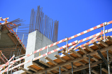 Fototapeta premium Concrete column with protruding rebar reinforcement bars and striped barrier tape at construction site, industrial building framework under sky