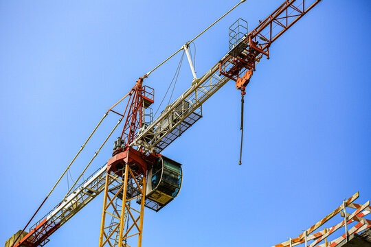 Tower crane with operator cabin and hook against clear sky at construction site, industrial machinery lifting equipment for building project closeup