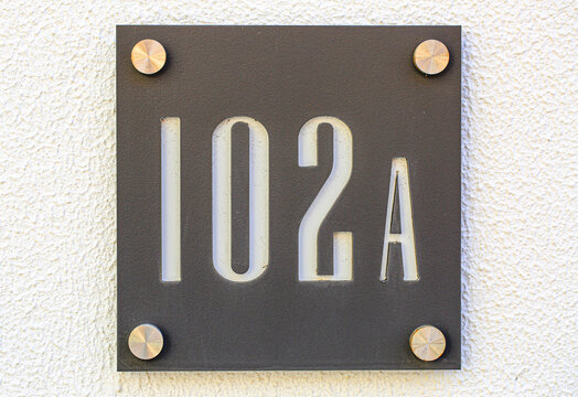 102A apartment number plate mounted with screws on textured wall, modern metal signage displaying unit address in minimalist industrial design